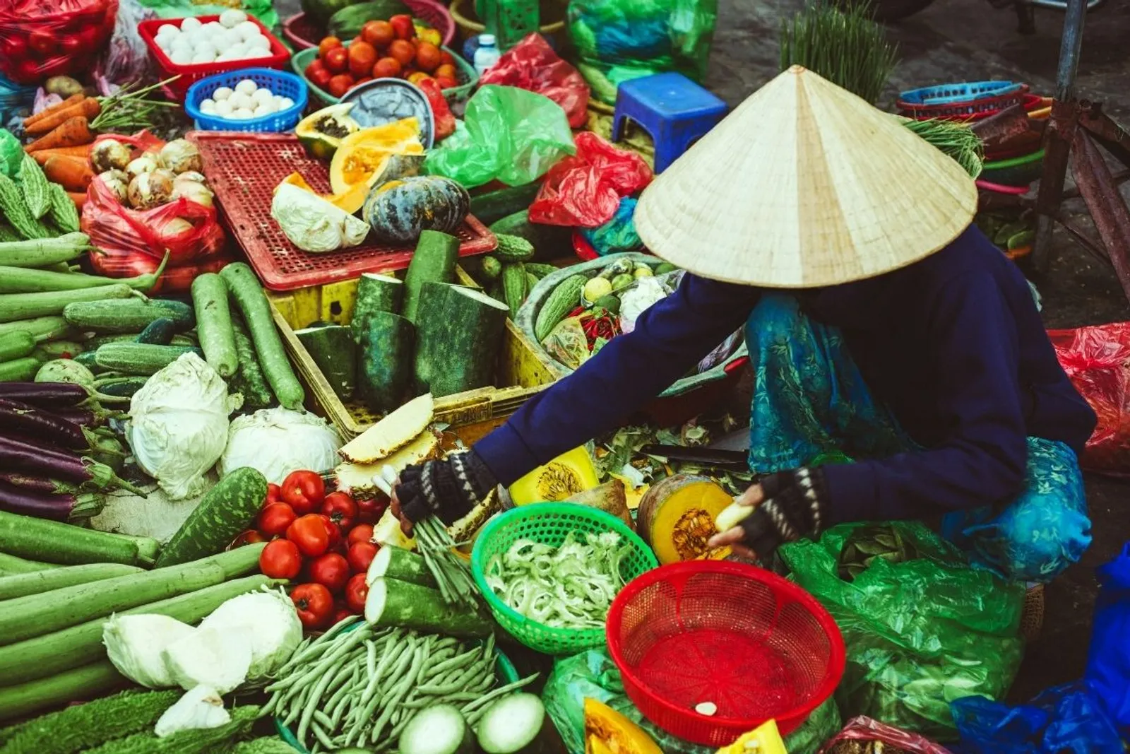 Vendor in a conical hat selling vegetables at a Hanoi market